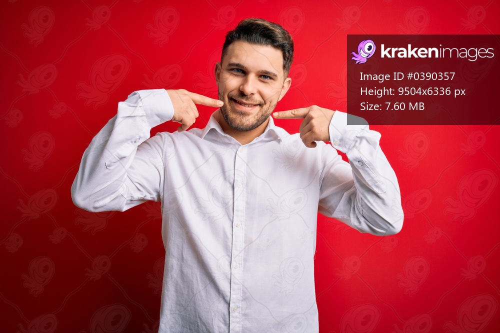 Young business man with blue eyes wearing elegant shirt standing over red isolated background smiling cheerful showing and pointing with fingers teeth and mouth. Dental health concept.