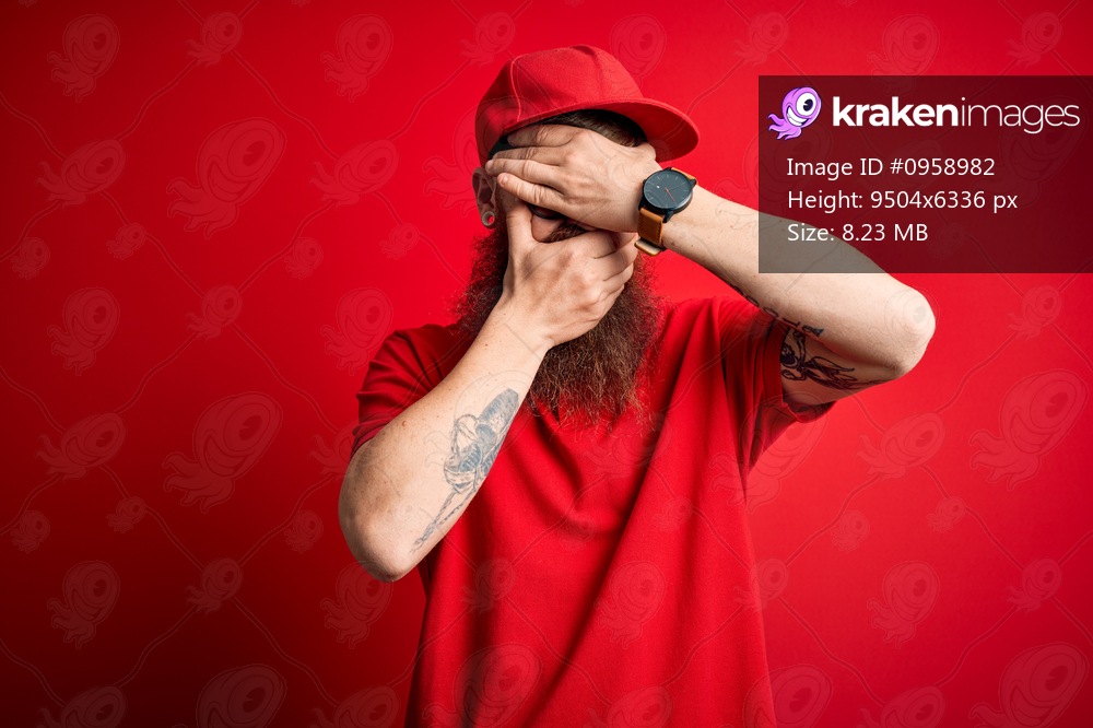 Young handsome delivery man wearing glasses and red cap over isolated background Covering eyes and mouth with hands, surprised and shocked. Hiding emotion