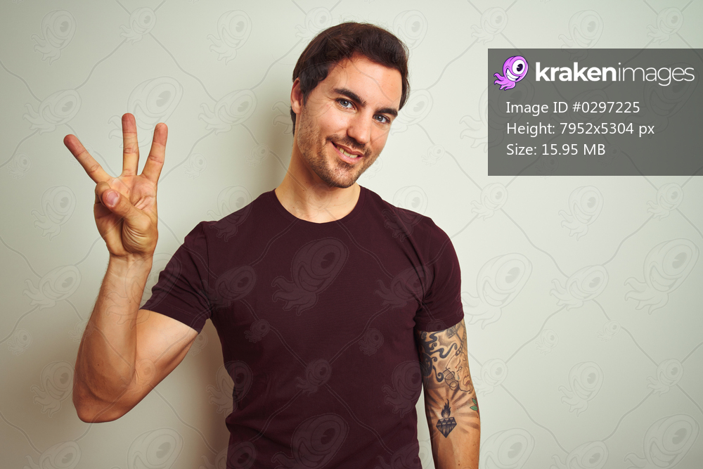 Young handsome man with tattoo wearing purple casual t-shirt over isolated white background showing and pointing up with fingers number three while smiling confident and happy.