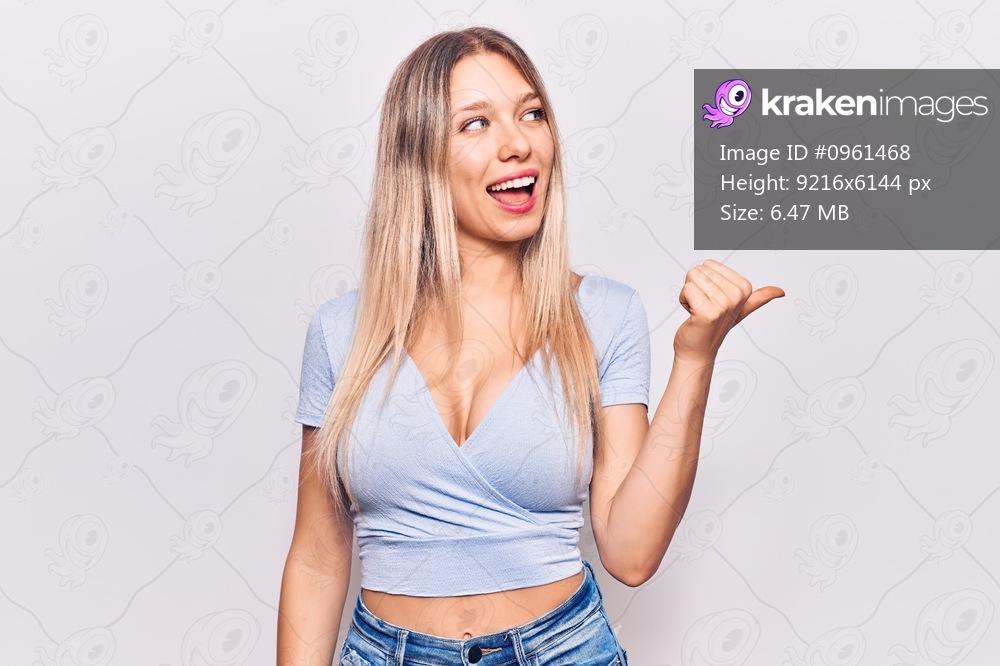 Young blonde woman wearing casual clothes pointing thumb up to the side smiling happy with open mouth 