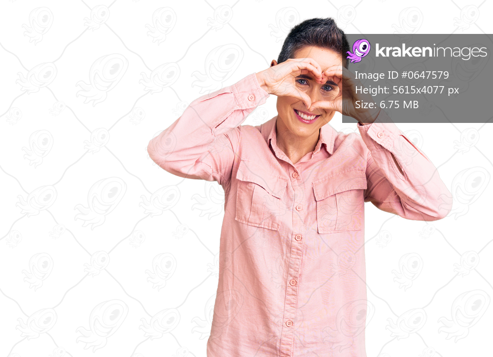 Young woman with short hair wearing casual clothes doing heart shape with hand and fingers smiling looking through sign 