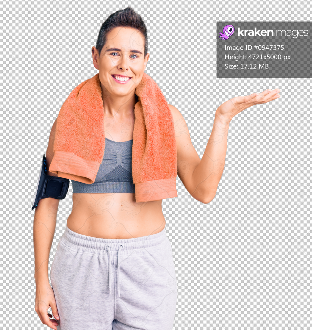 Young woman with short hair wearing sportswear and towel using smartphone smiling cheerful presenting and pointing with palm of hand looking at the camera.