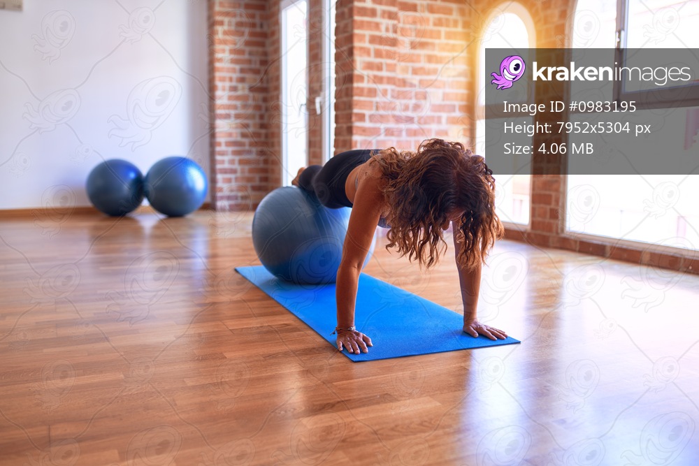 Middle age beautiful sportswoman doing exercise using fitness ball in a class of yoga at gym