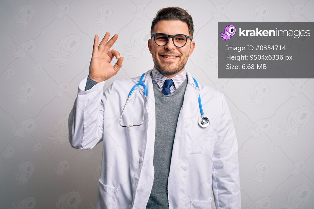 Young doctor man with blue eyes wearing medical coat and stethoscope over isolated background smiling positive doing ok sign with hand and fingers. Successful expression.