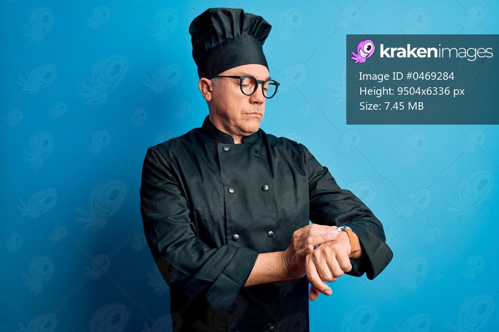 Middle age handsome grey-haired chef man wearing cooker uniform and hat Checking the time on wrist watch, relaxed and confident