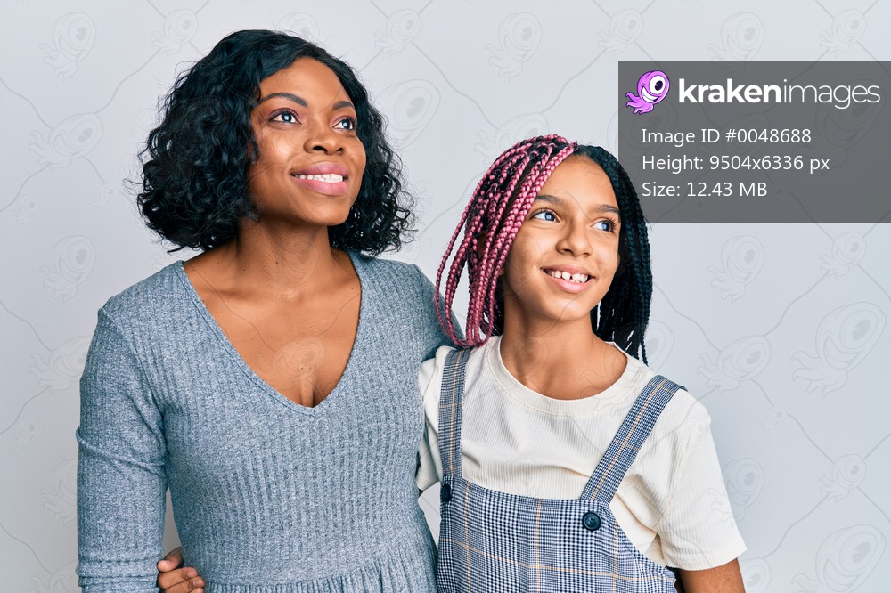 Beautiful african american mother and daughter wearing casual clothes and hugging smiling looking to the side and staring away thinking. 