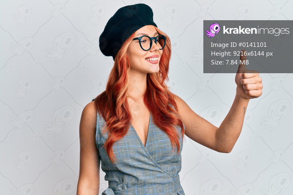 Young redhead woman wearing fashion french look with beret looking proud, smiling doing thumbs up gesture to the side 