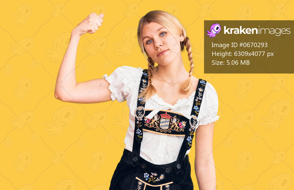 Young beautiful blonde woman wearing oktoberfest dress strong person showing arm muscle, confident and proud of power 
