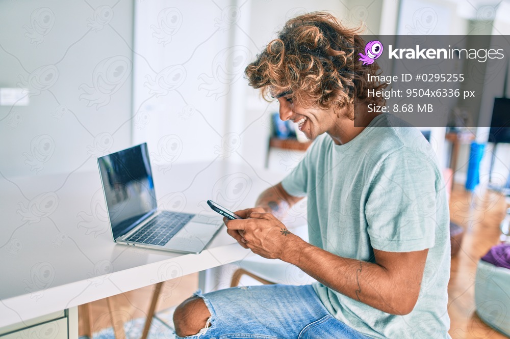 Young hispanic man smiling happy using smartphone sitting on the table at home