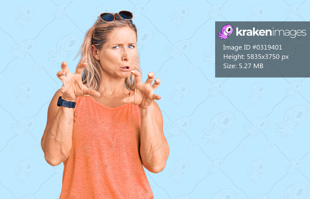 Middle age fit blonde woman wearing casual summer clothes and sunglasses smiling funny doing claw gesture as cat, aggressive and sexy expression 