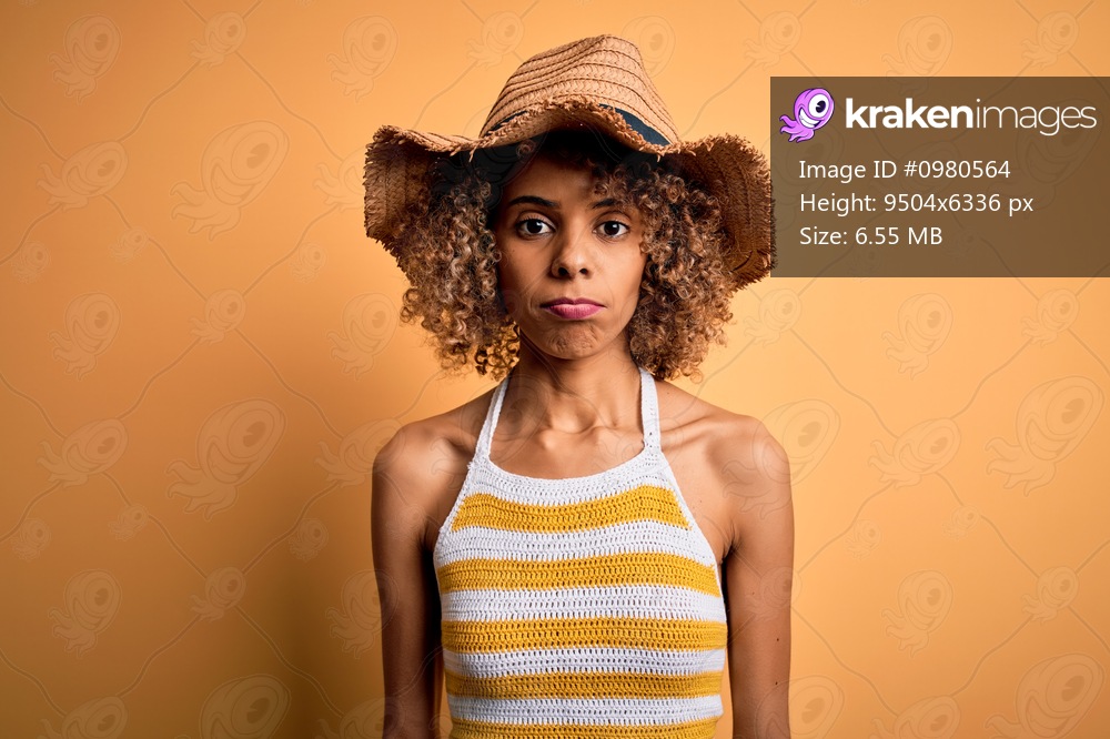 African american tourist woman with curly on vacation wearing summer hat and striped t-shirt depressed and worry for distress, crying angry and afraid. Sad expression.