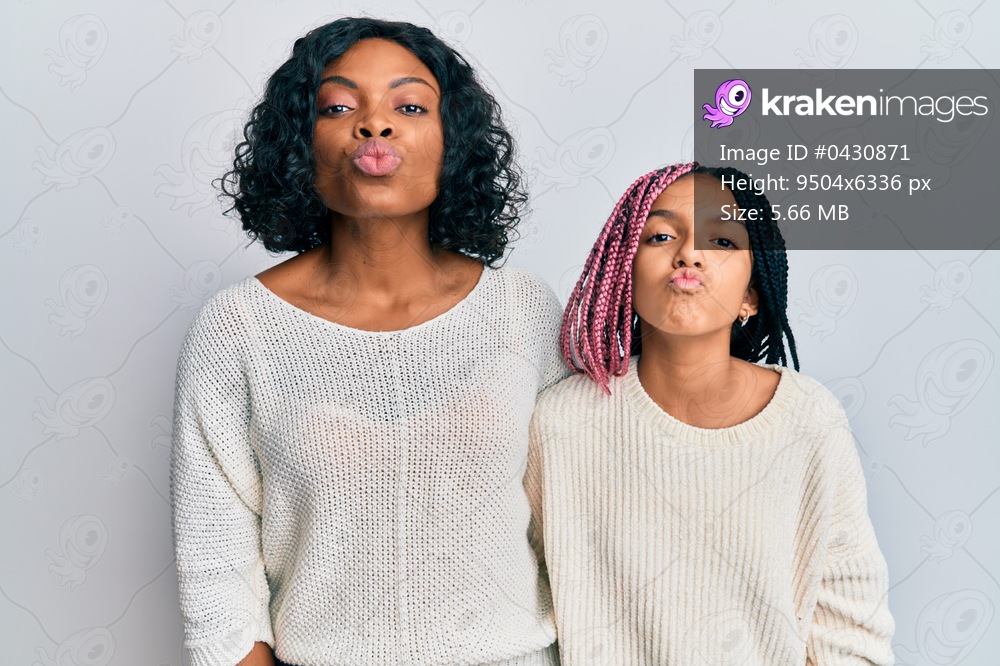 Beautiful african american mother and daughter wearing casual clothes and hugging looking at the camera blowing a kiss on air being lovely and sexy. love expression. 