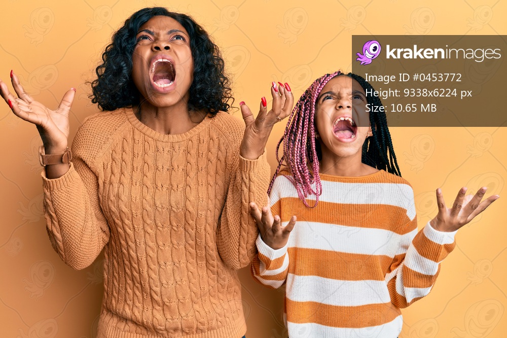 Beautiful african american mother and daughter wearing wool winter sweater crazy and mad shouting and yelling with aggressive expression and arms raised. frustration concept. 