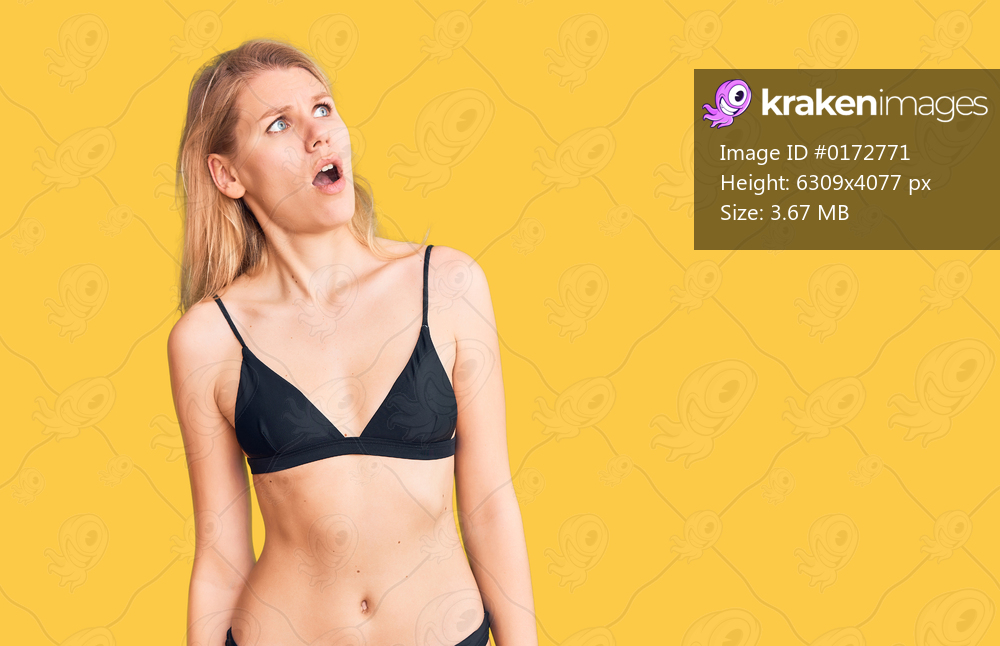 Young beautiful blonde woman wearing bikini in shock face, looking skeptical and sarcastic, surprised with open mouth 