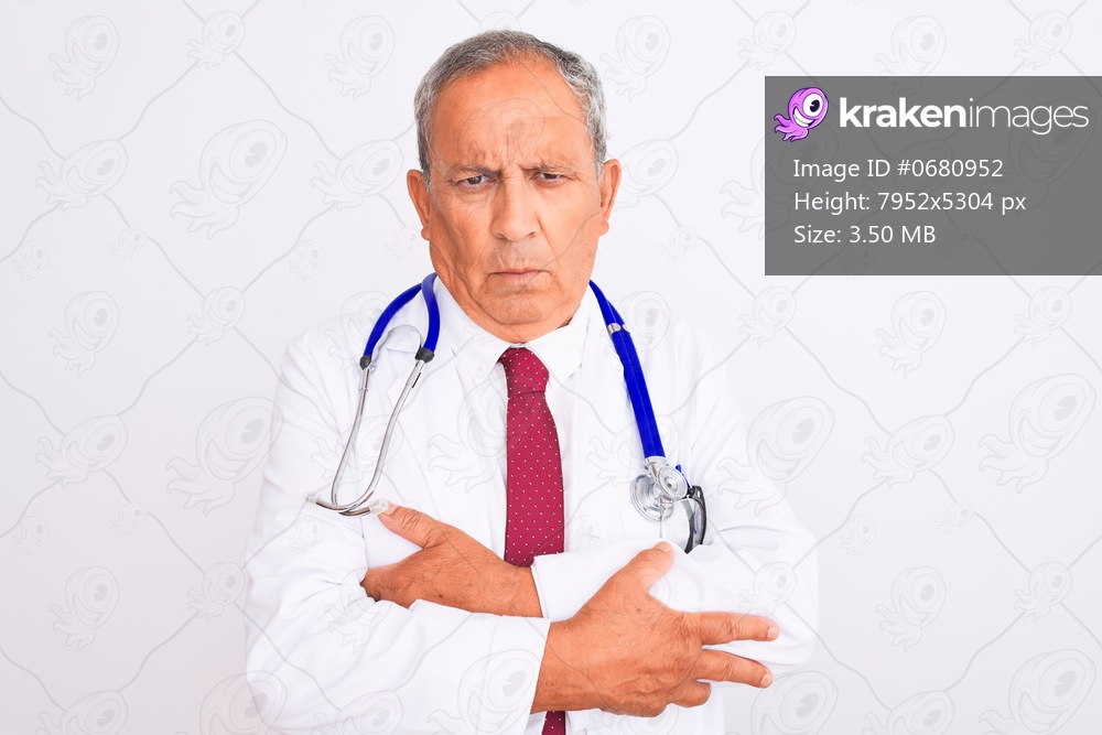Senior grey-haired doctor man wearing stethoscope standing over isolated white background skeptic and nervous, disapproving expression on face with crossed arms. Negative person.