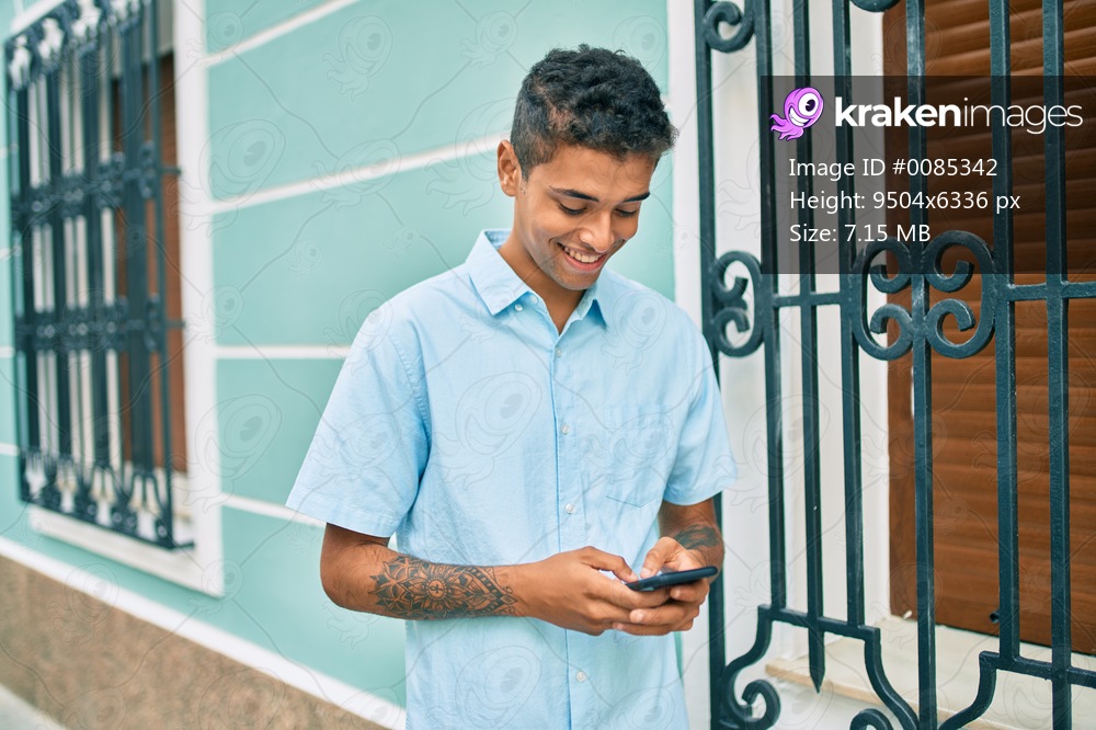 Young latin man smiling happy using smartphone walking at the city.