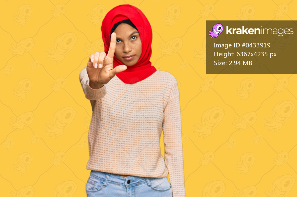 Young african american woman wearing traditional islamic hijab scarf pointing with finger up and angry expression, showing no gesture 