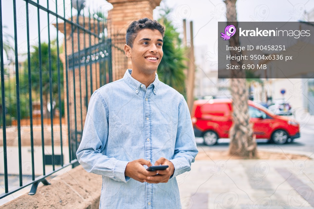 Young latin man smiling happy using smartphone walking at the city.