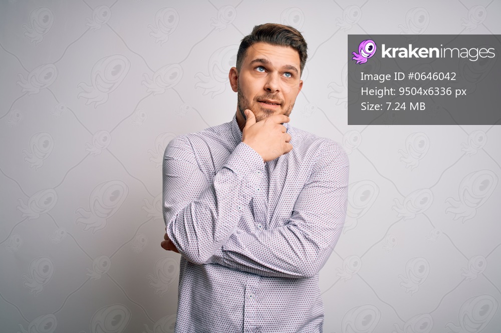 Young business man with blue eyes standing over isolated background with hand on chin thinking about question, pensive expression. Smiling with thoughtful face. Doubt concept.