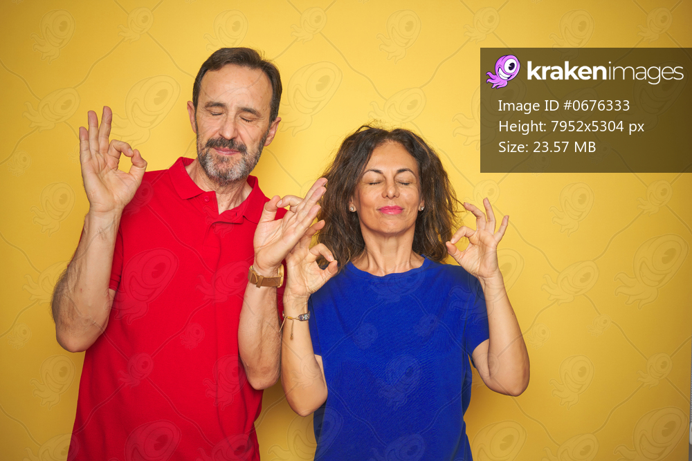 Beautiful middle age couple together standing over isolated yellow background relax and smiling with eyes closed doing meditation gesture with fingers. Yoga concept.