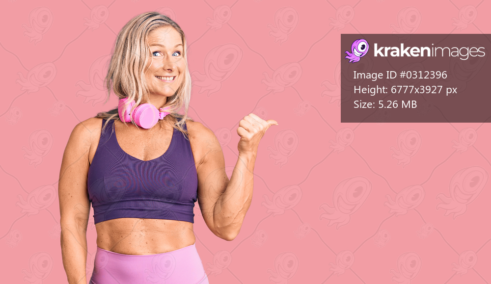 Middle age fit blonde woman wearing gym clothes and using headphones smiling with happy face looking and pointing to the side with thumb up. 