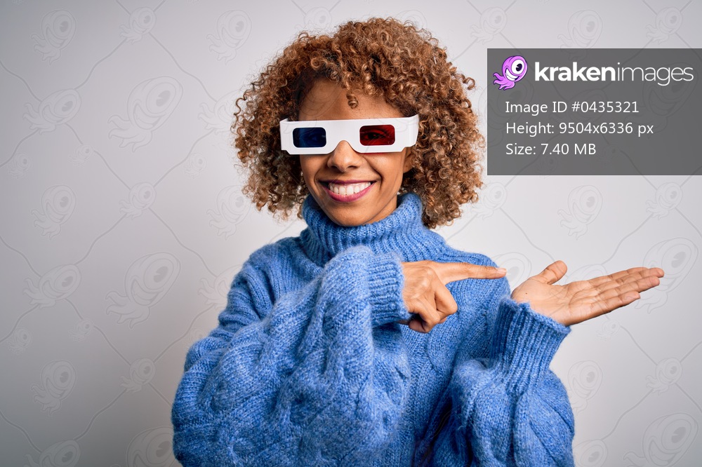 Young african american curly woman wearing 3d glasses over isolated white background amazed and smiling to the camera while presenting with hand and pointing with finger.