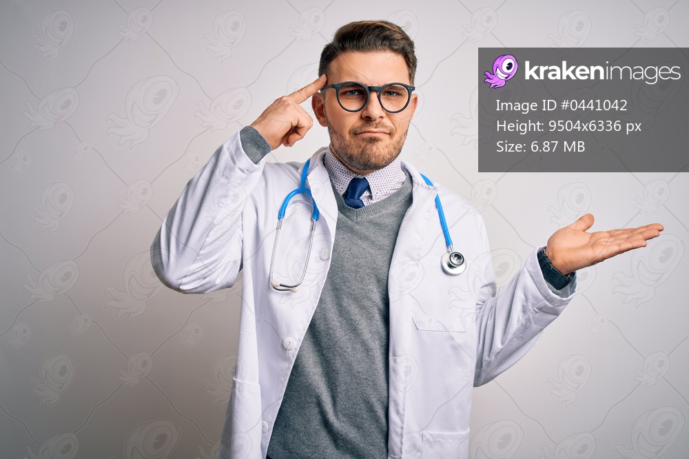Young doctor man with blue eyes wearing medical coat and stethoscope over isolated background confused and annoyed with open palm showing copy space and pointing finger to forehead. Think about it.