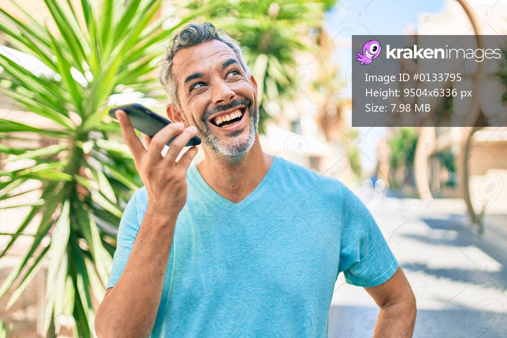 Middle age grey-haired man talking on the smartphone walking at street of city.
