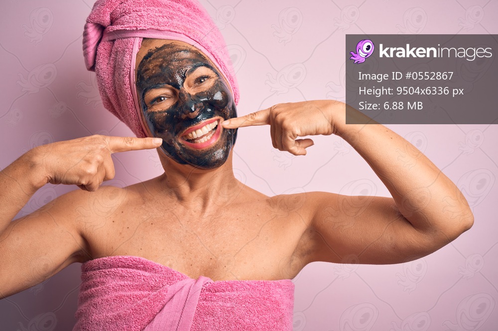 Middle age brunette woman wearing beauty black face mask over isolated pink background smiling cheerful showing and pointing with fingers teeth and mouth. Dental health concept.