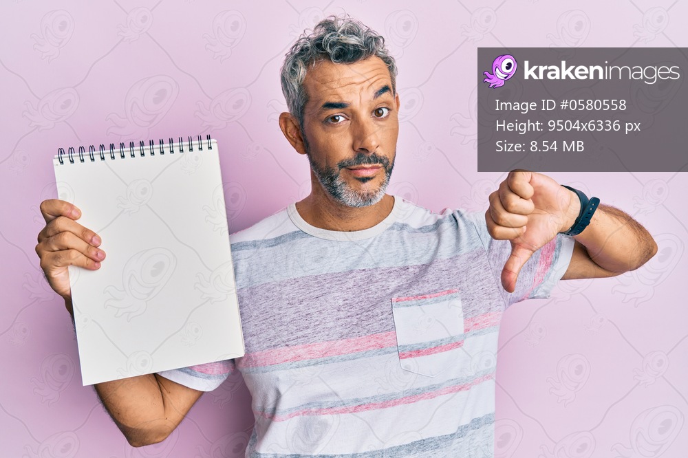 Middle age grey-haired man holding empty notebook with angry face, negative sign showing dislike with thumbs down, rejection concept 