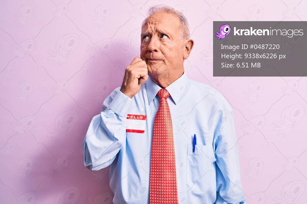 Senior handsome grey-haired businessman wearing tie and shirt with name presentation sticker thinking concentrated about doubt with finger on chin and looking up wondering