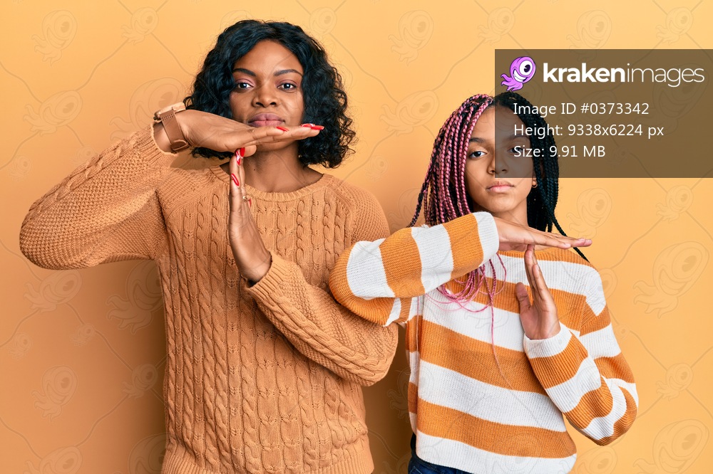 Beautiful african american mother and daughter wearing wool winter sweater doing time out gesture with hands, frustrated and serious face 