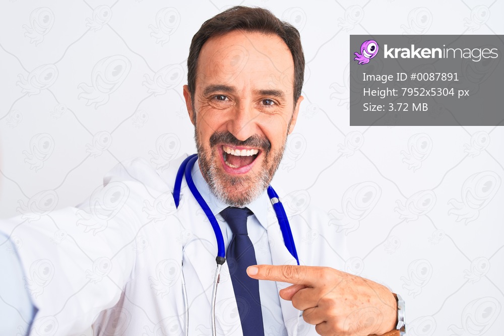 Middle age doctor man wearing stethoscope make selfie over isolated white background very happy pointing with hand and finger