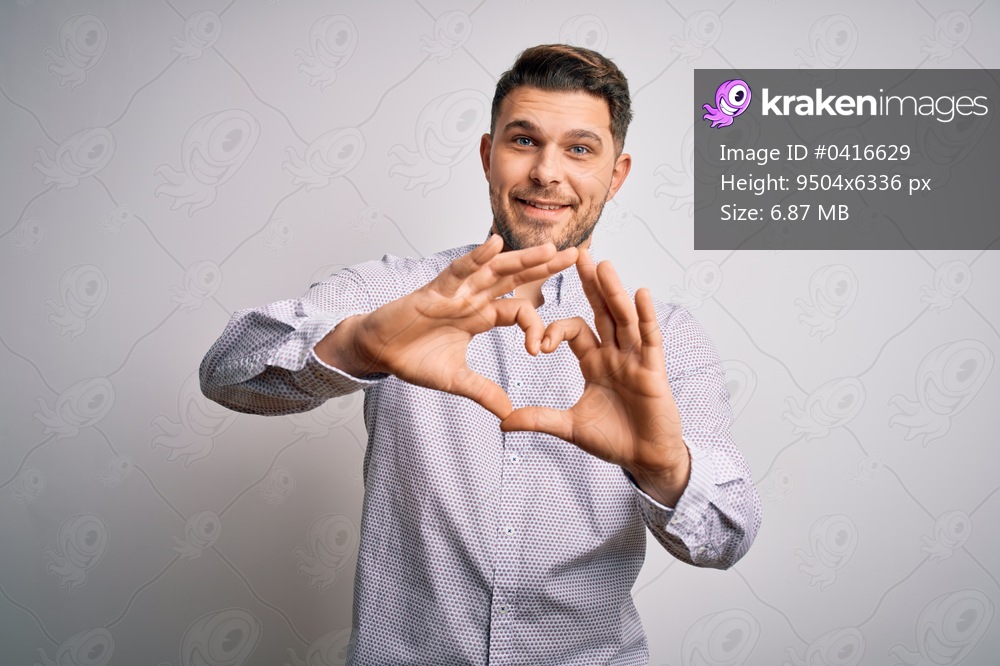 Young business man with blue eyes standing over isolated background smiling in love doing heart symbol shape with hands. Romantic concept.