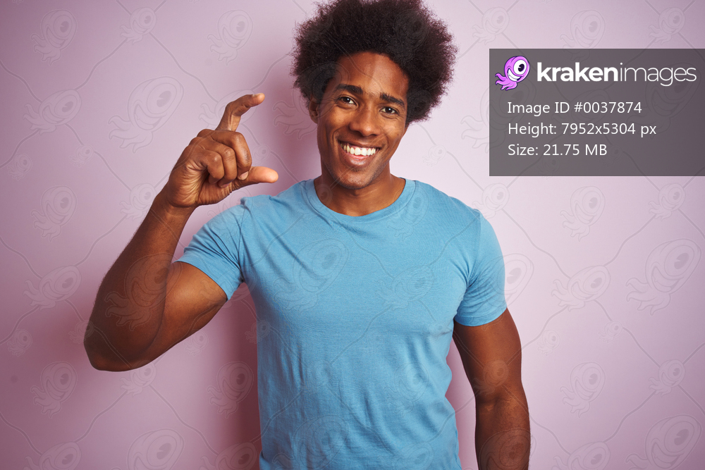 African american man with afro hair wearing blue t-shirt standing over isolated pink background smiling and confident gesturing with hand doing small size sign with fingers looking and the camera. Measure concept.
