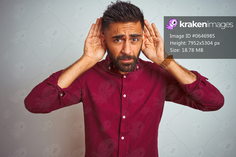 Young indian man wearing red elegant shirt standing over isolated grey background Trying to hear both hands on ear gesture, curious for gossip. Hearing problem, deaf