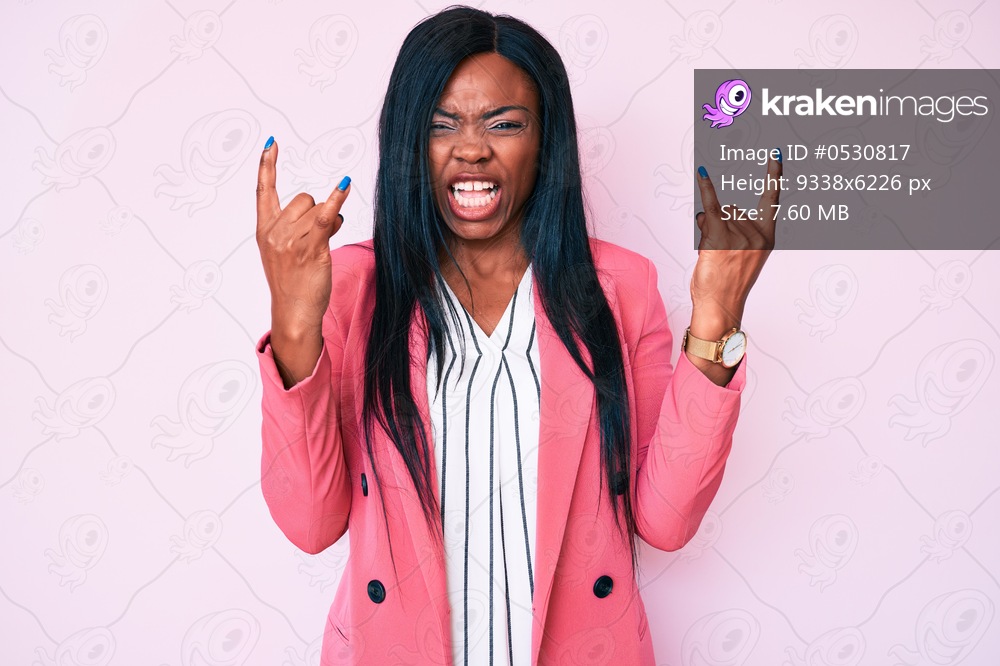 Young african american woman wearing business clothes shouting with crazy expression doing rock symbol with hands up. music star. heavy concept. 