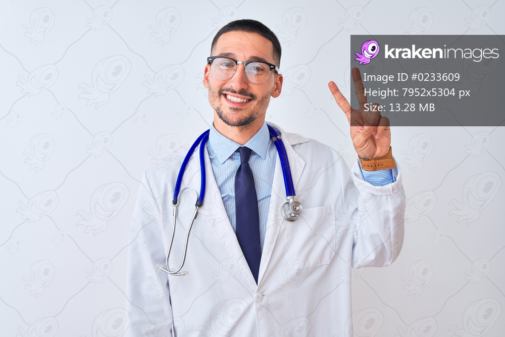 Young doctor man wearing stethoscope over isolated background smiling looking to the camera showing fingers doing victory sign. Number two.