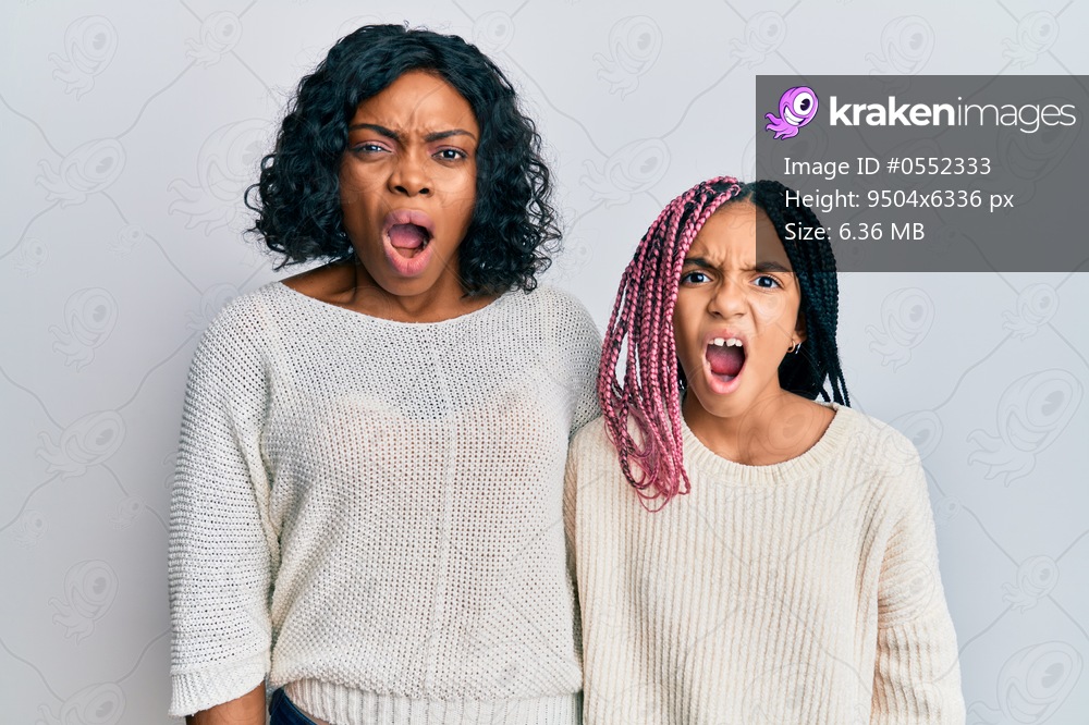 Beautiful african american mother and daughter wearing casual clothes and hugging in shock face, looking skeptical and sarcastic, surprised with open mouth 