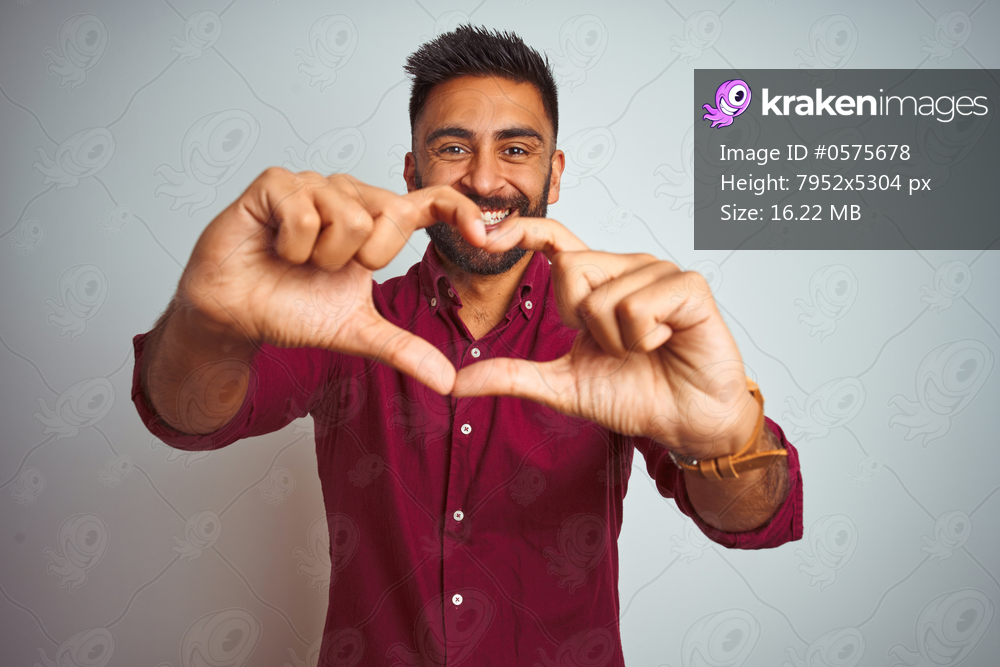 Young indian man wearing red elegant shirt standing over isolated grey background smiling in love doing heart symbol shape with hands. Romantic concept.