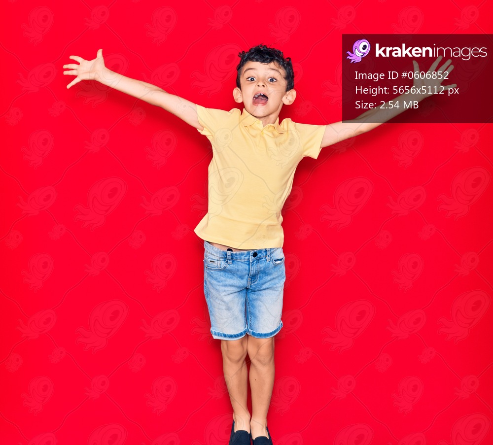 Adorable kid wearing casual clothes jumping over isolated red background