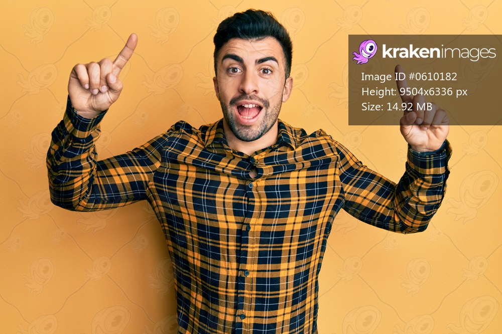 Young hispanic man wearing casual clothes smiling amazed and surprised and pointing up with fingers and raised arms. 