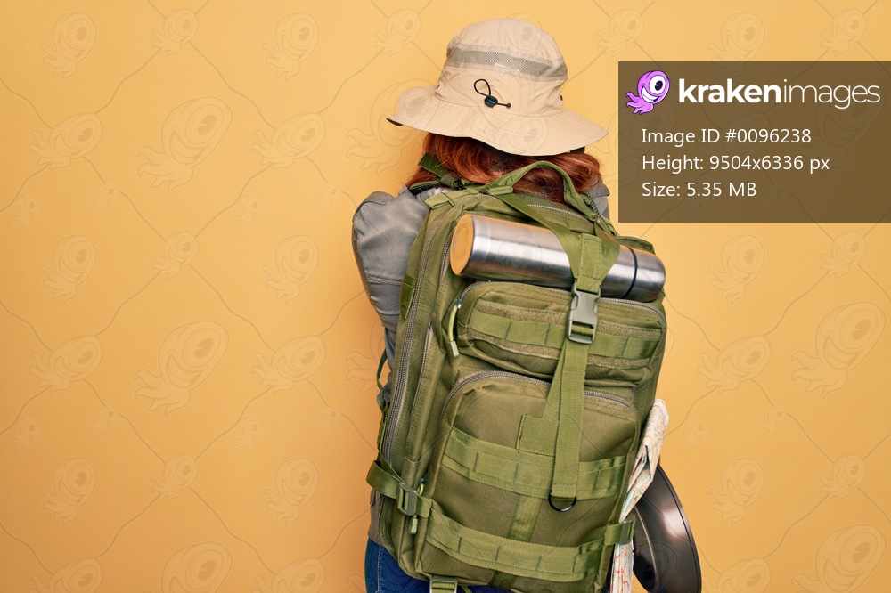 Young redhead backpacker woman hiking wearing backpack and hat over yellow background Hugging oneself happy and positive from backwards. Self love and self care
