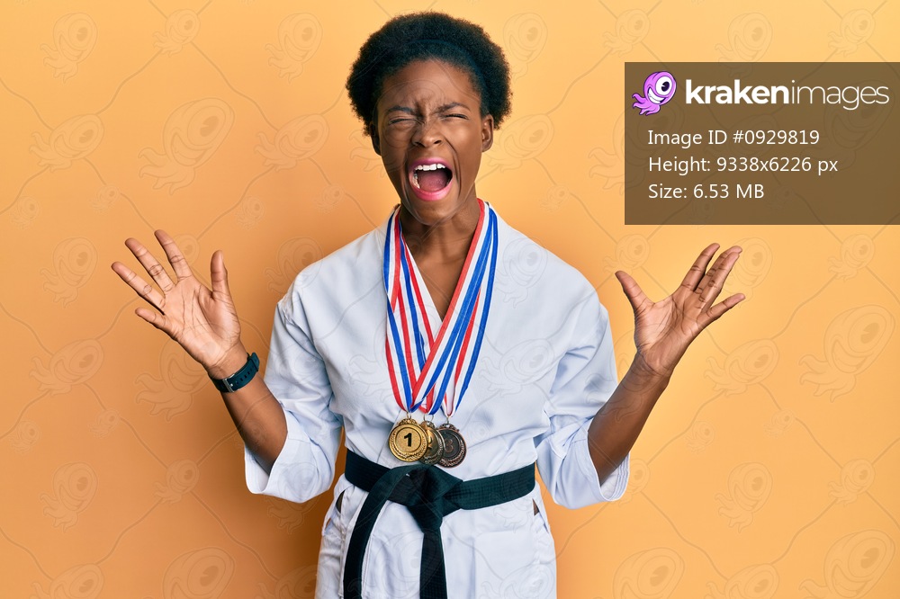 Young african american girl wearing karate kimono and black belt celebrating mad and crazy for success with arms raised and closed eyes screaming excited. winner concept 