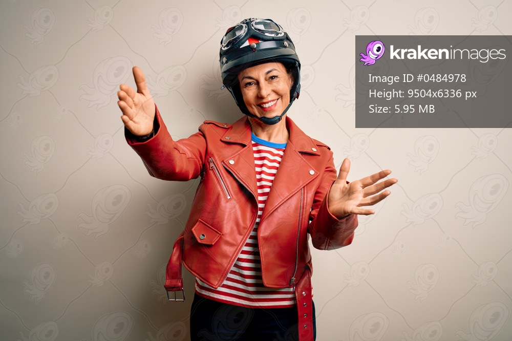 Middle age motorcyclist woman wearing motorcycle helmet and jacket over white background looking at the camera smiling with open arms for hug. Cheerful expression embracing happiness.