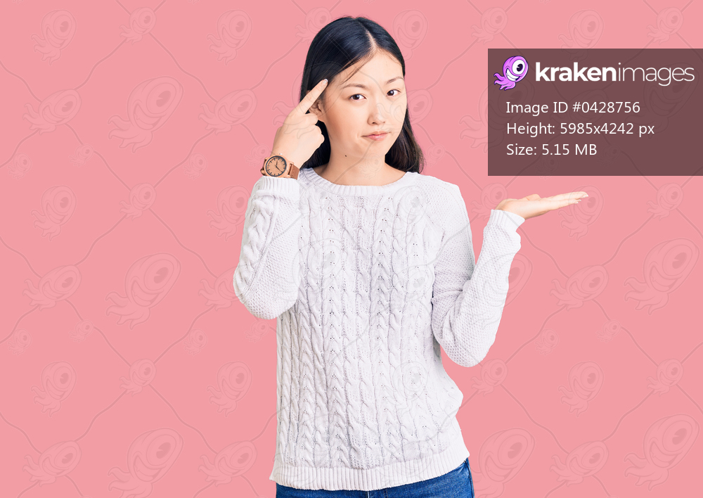 Young beautiful chinese woman wearing casual sweater confused and annoyed with open palm showing copy space and pointing finger to forehead. think about it. 