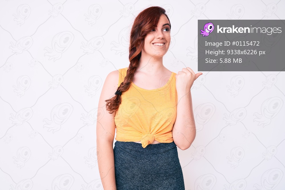 Young beautiful woman wearing casual clothes pointing thumb up to the side smiling happy with open mouth 
