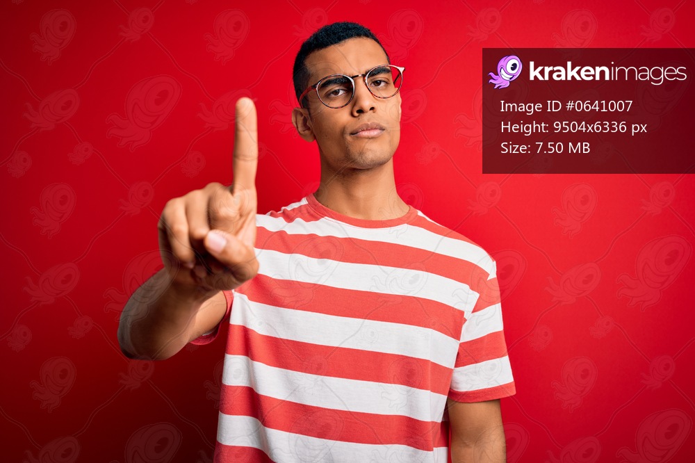 Young handsome african american man wearing casual striped t-shirt and glasses Pointing with finger up and angry expression, showing no gesture