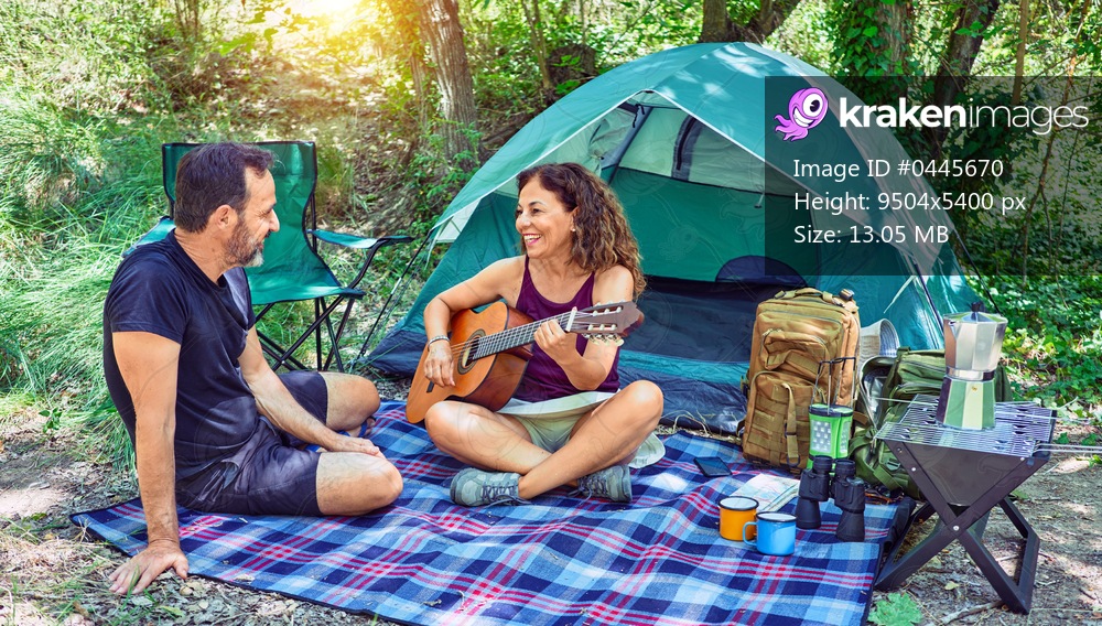 Middle age couple  of hiker smiling happy camping at the forest. Sitting on the floor singing song playing classical guitar