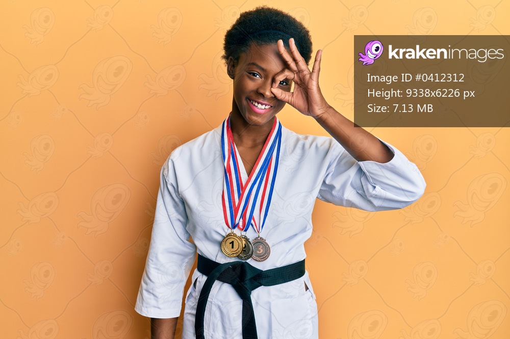 Young african american girl wearing karate kimono and black belt smiling happy doing ok sign with hand on eye looking through fingers 